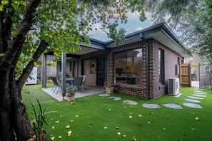 Una casa moderna con fachada de ladrillo, ventanas grandes y un patio con mobiliario exterior.