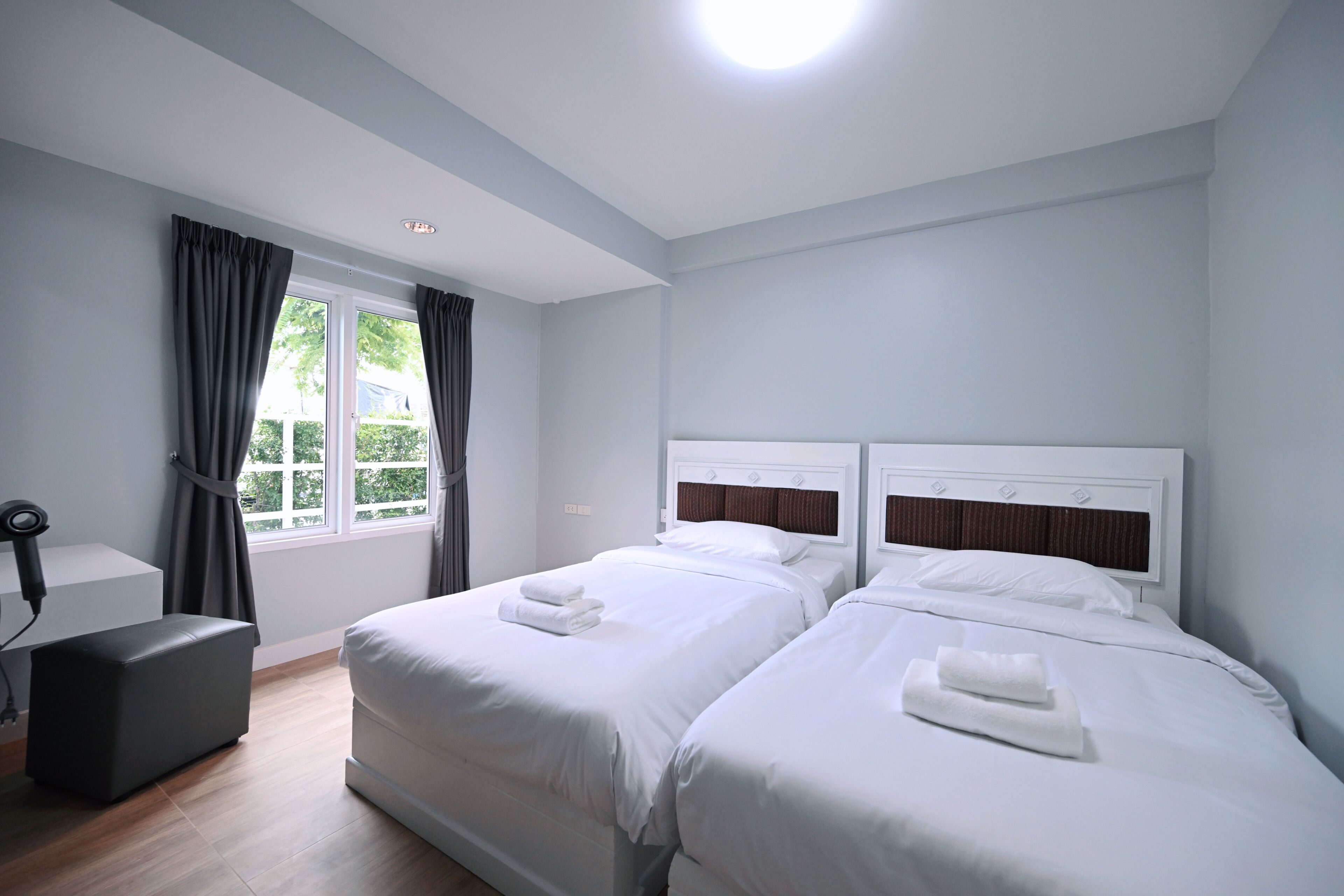 A hotel room with two beds, a desk, and a window with curtains.