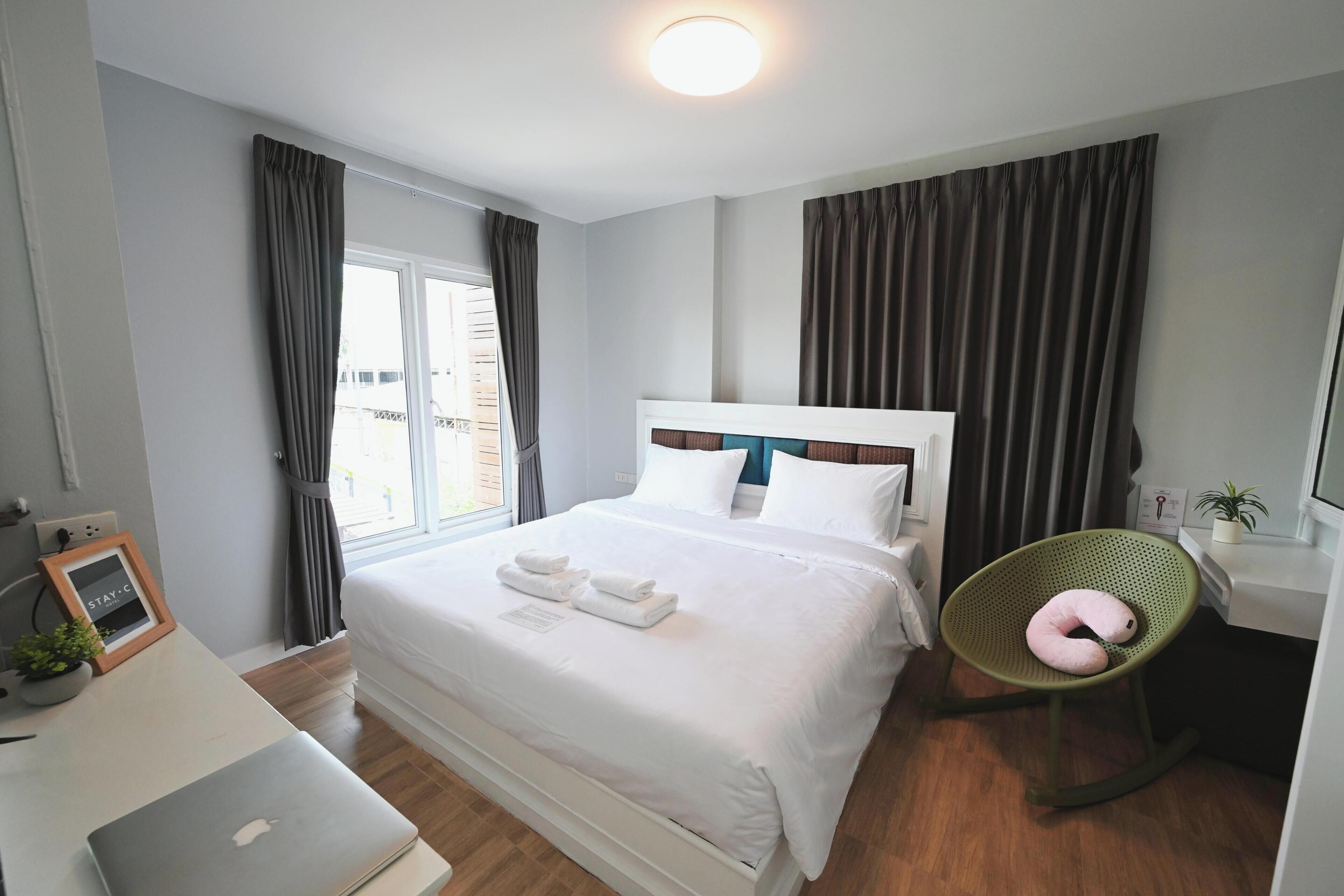 A hotel room with a bed, a desk with a laptop, a chair, and a window with curtains.