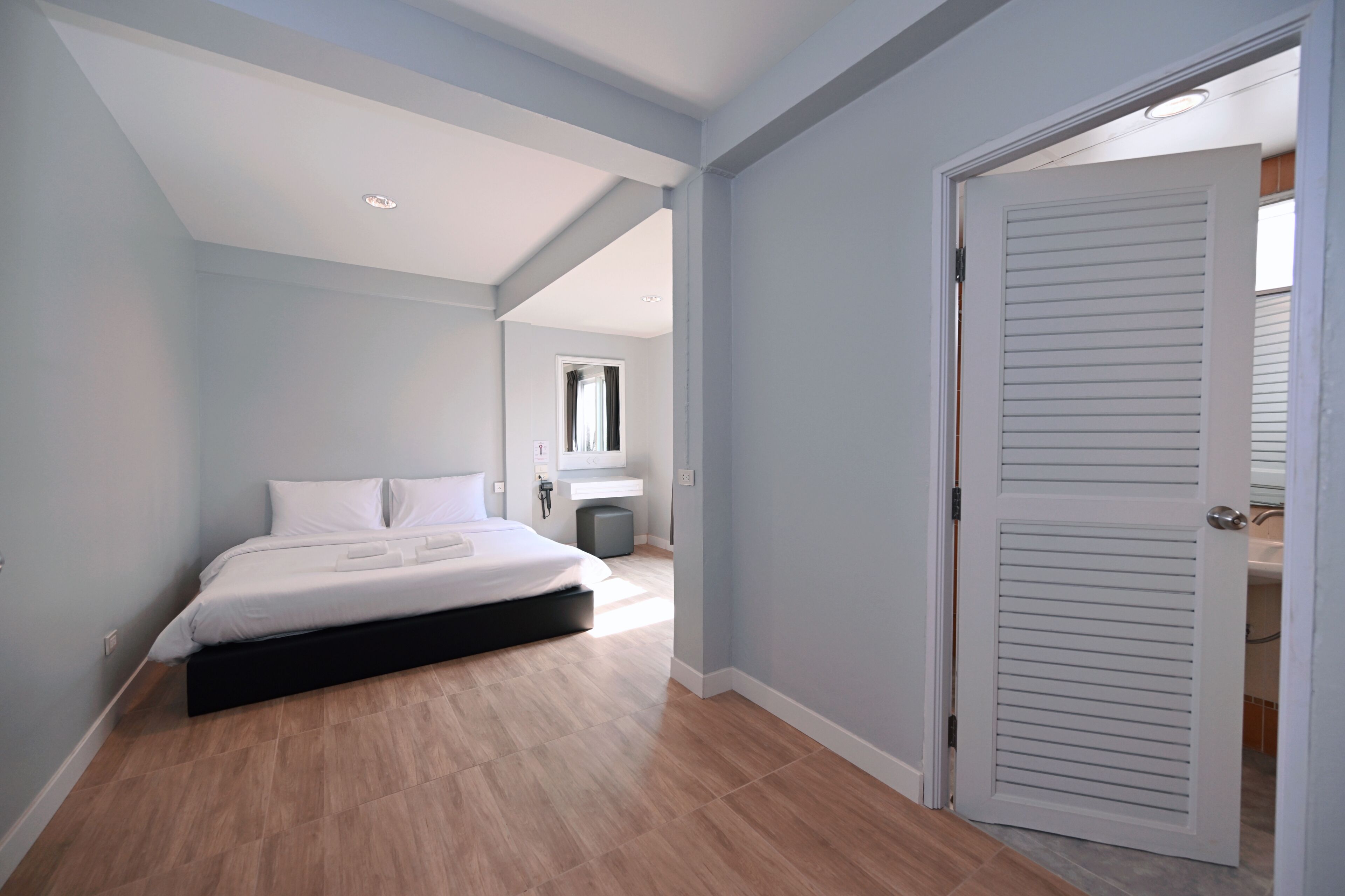 A bedroom with a bed, a bedside table, and a door leading to another room.