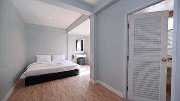 A bedroom with a bed, a bedside table, and a door leading to another room.