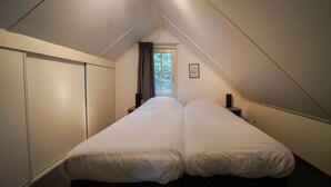 Un pequeño dormitorio en el ático, tenuemente iluminado, con una cama individual, una ventana y un armario.
