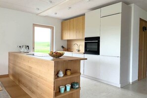 Une cuisine moderne avec des meubles en bois, un îlot central intégré et une vue sur l’extérieur.