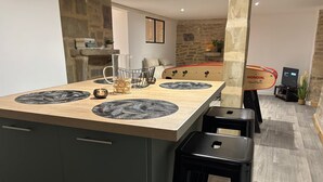 Een moderne keuken met een centraal kookeiland, zwarte barkrukken en een stenen muur op de achtergrond.