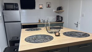 Een keuken met een houten aanrecht, zwarte placemats, een zwarte koffiezetapparaat en een magnetron boven een witte koelkast.