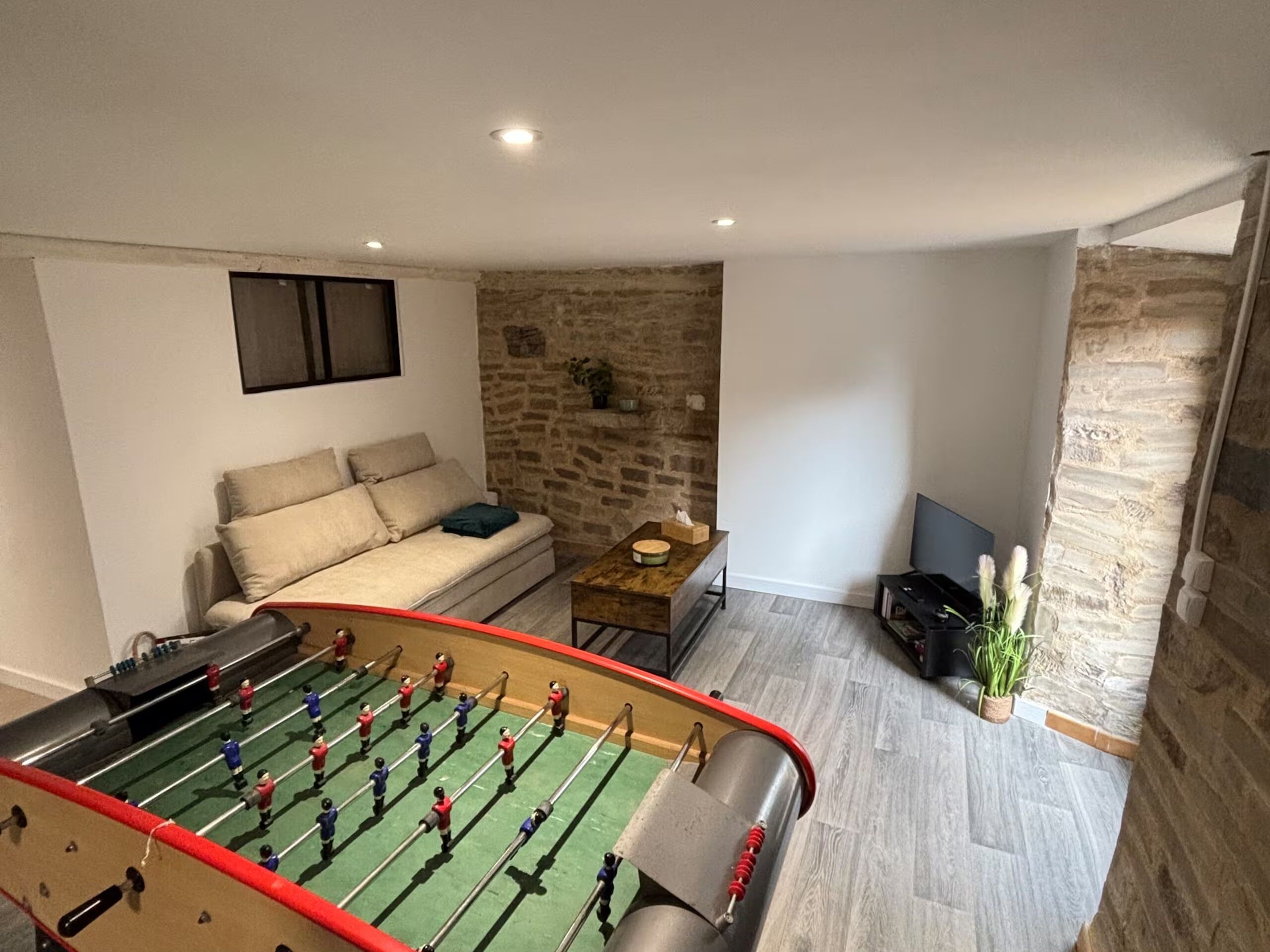 A living room with a foosball table, a sofa, a coffee table, and a stone wall.