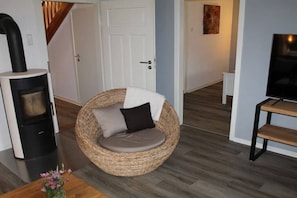 Ein Zimmer mit einem runden Korbstuhl, einem Fernsehschrank, einem Kamin und einer Tür zu einem anderen Raum.