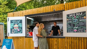 En food truck med en meny på en anslagstavla, en skylt för glass och ett trästaket.