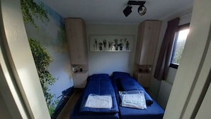 Habitació amb dos llits, un mural a la paret, un ventilador al sostre i una finestra amb cortines.