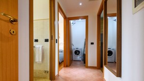 Un pasillo con puerta de madera, piso de baldosas y zona de lavandería con lavadoras.