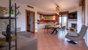 Una sala moderna con un sofá, una mesa de comedor y sillas. Se observa una cocina en el fondo con armarios y una estufa.