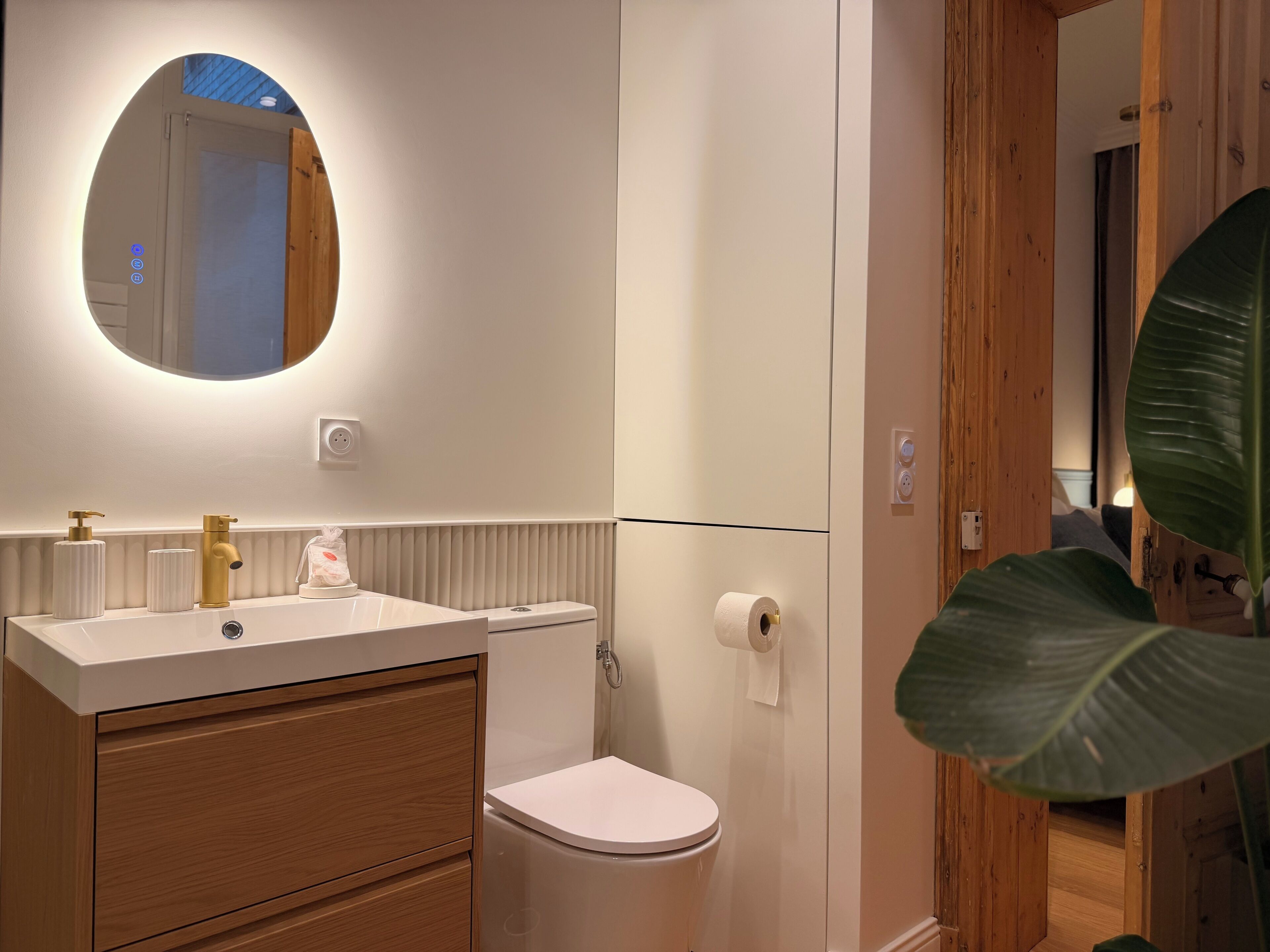 A modern bathroom with a white sink, gold faucet, and a mirror above it.