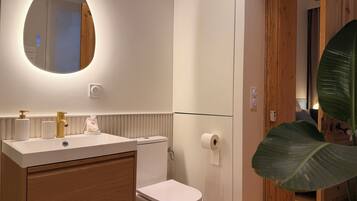 A modern bathroom with a white sink, gold faucet, and a mirror above it.