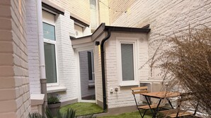 A small courtyard with a wooden table and chairs, a potted plant, and a brick wall. - L'Échappée Malouine: Beach 3 min away + Private courtyard (Dunkerque)