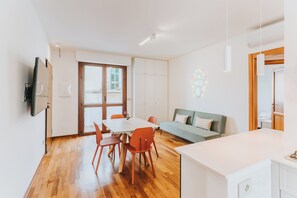 A modern living room with a dining area, wooden flooring, a sofa, and a TV mounted on the wall. - Casa Edoardo - Modern in Porta San Biagio (Lecce)