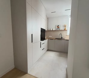 Moderni keittiö, jossa on valkoiset kaapit, musta uuni ja pesuallas.