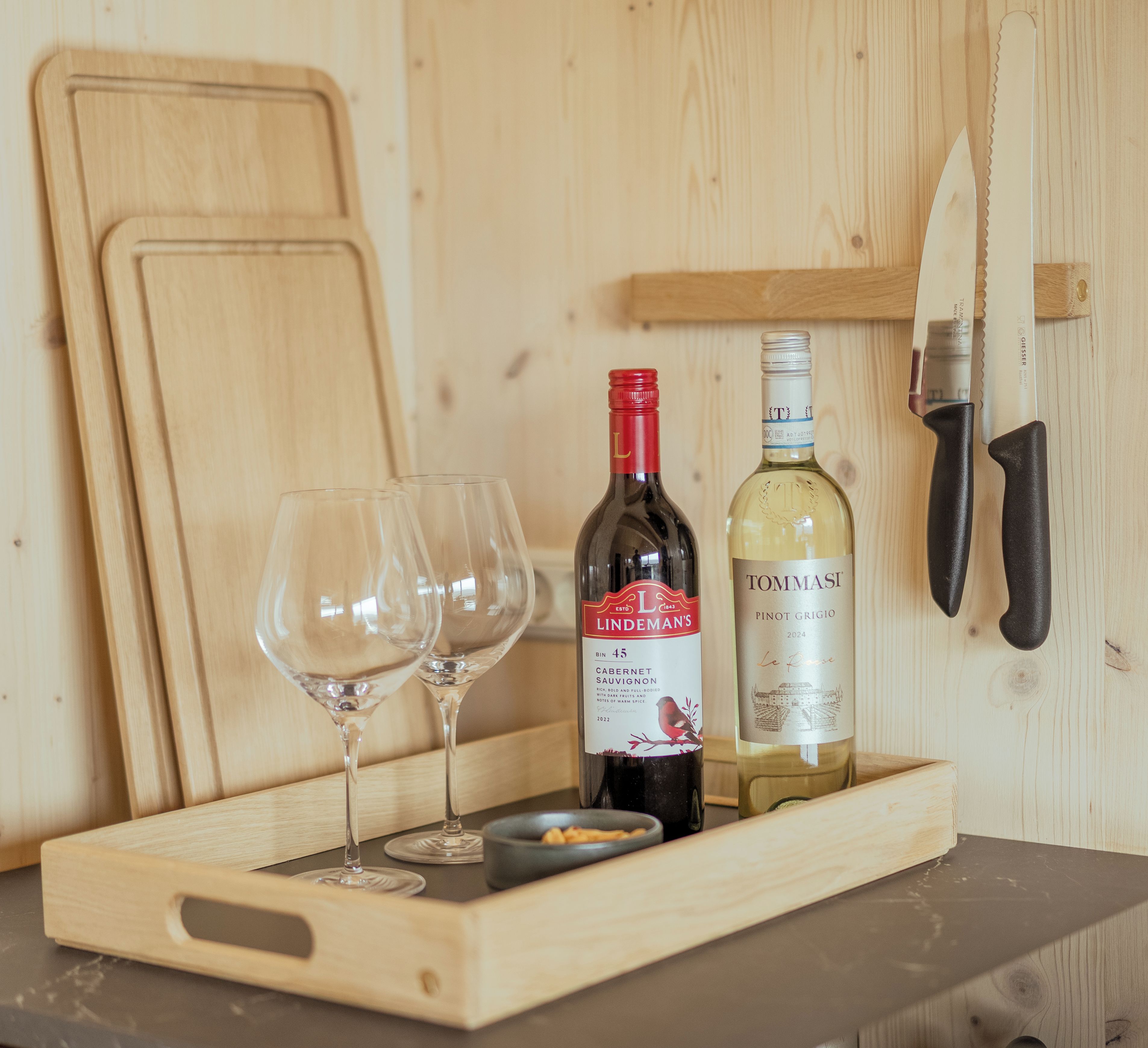 A wooden tray with two wine glasses, a bottle of Lindeman's Cabernet Sauvignon, and a bottle of Tommasi Pinot Grigio.