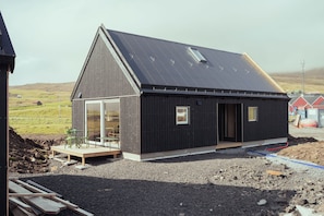 A modern building with a sloped roof, large windows, and a wooden deck. - The Lakehouse (Miðvágur)