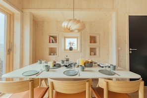 Comedor con mesa blanca, sillas de madera, lámpara colgante y vistas al exterior a través de una ventana.