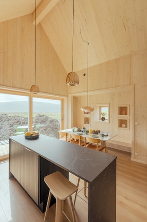 A modern kitchen with a large island, wooden cabinetry, and pendant lighting. - The Lakehouse (Miðvágur)