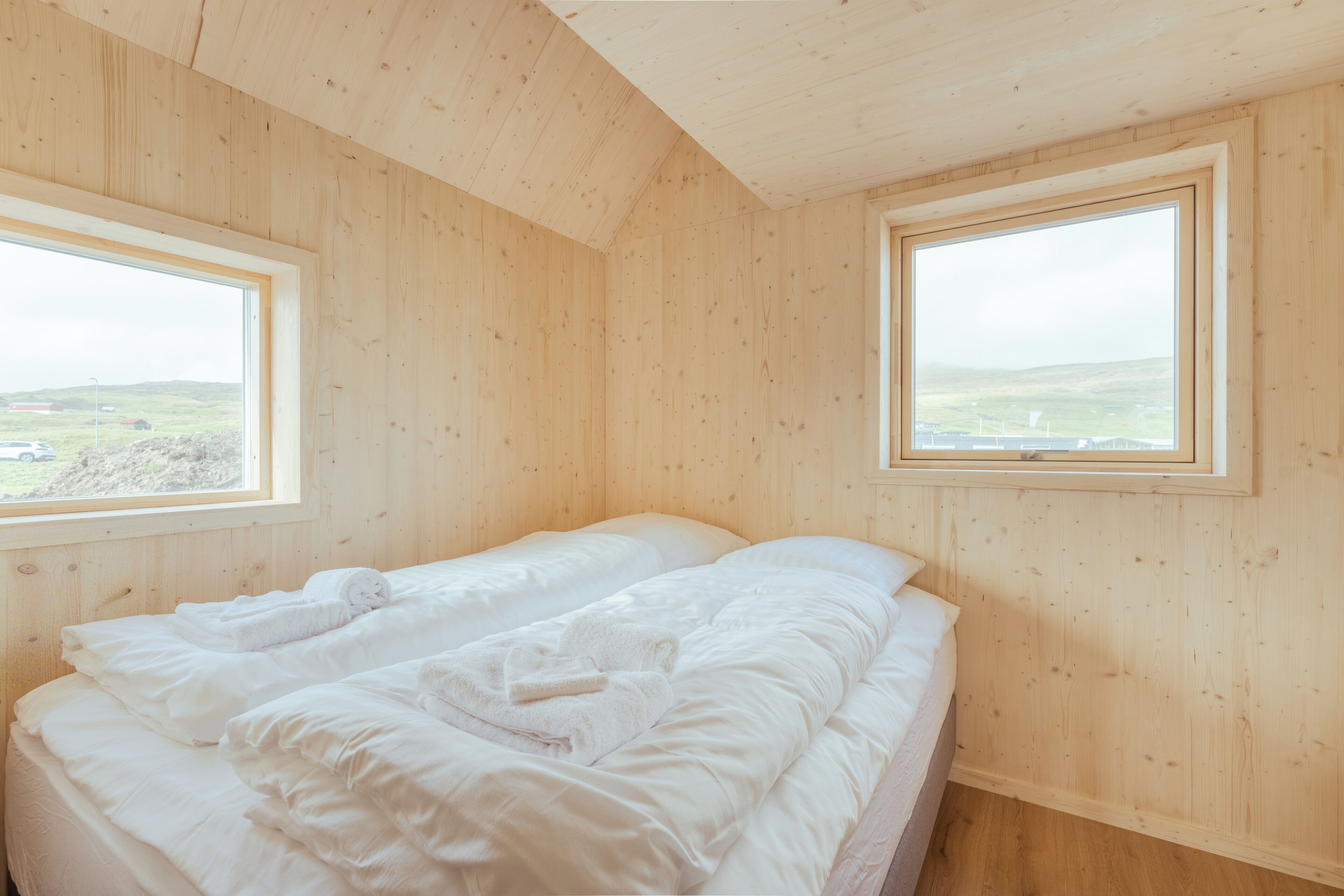 Une pièce en bois avec deux lits, de grandes fenêtres et une vue sur la campagne.