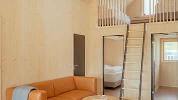 Ett rum i loftstil med ett träpanelat tak, en soffa, ett soffbord, en stege och en våningssäng.