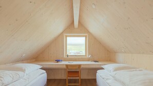 Une petite pièce en bois, avec deux lits, un bureau et une fenêtre.