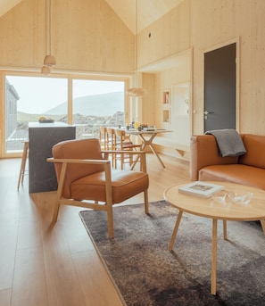 A spacious living area with a dining table, chairs, a sofa, and a coffee table. - The Lakehouse (Miðvágur)