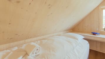 A room with a wooden ceiling, a bed with white bedding, a small window, and a book on a shelf.