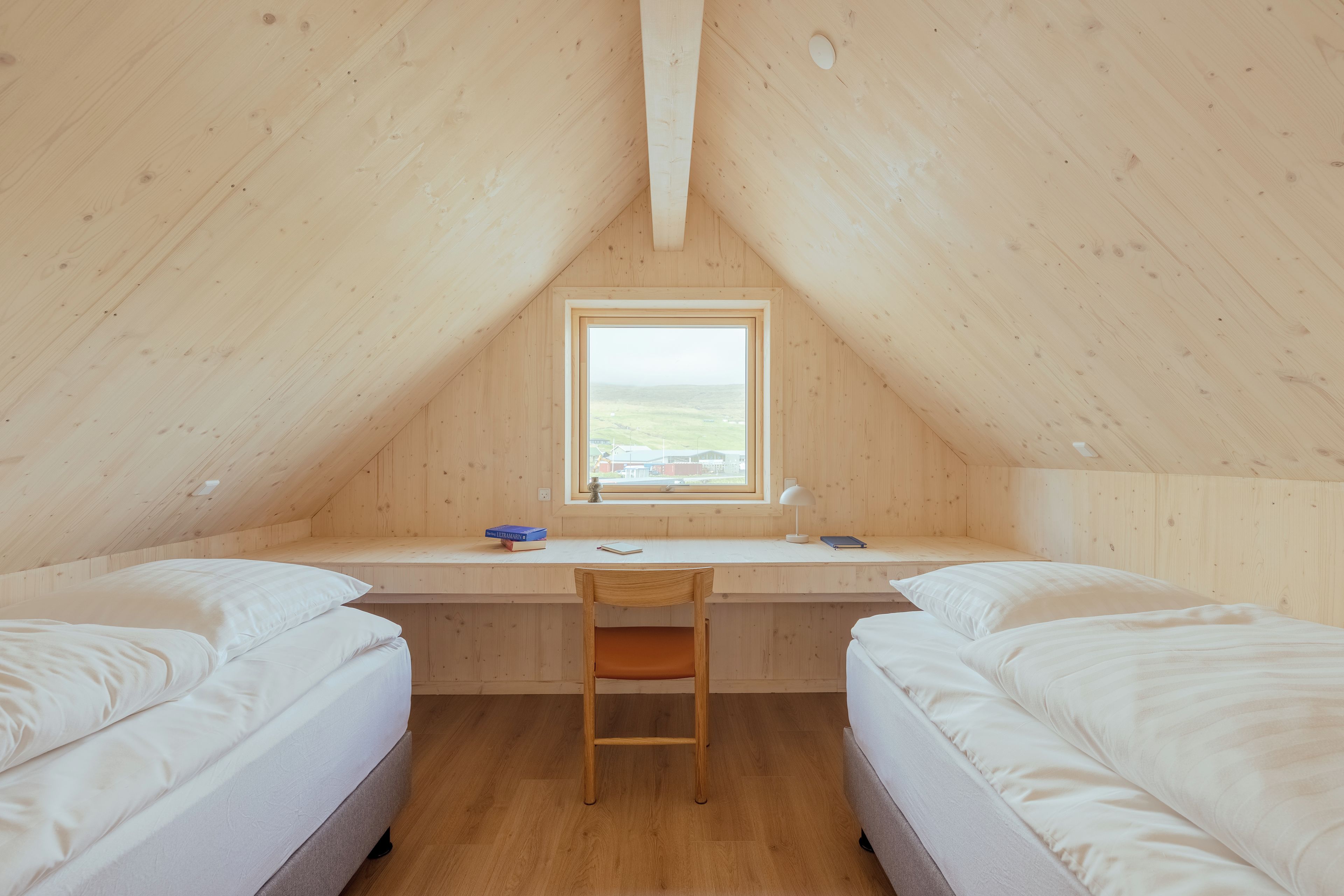 A small, wooden room with two beds, a desk, and a window.