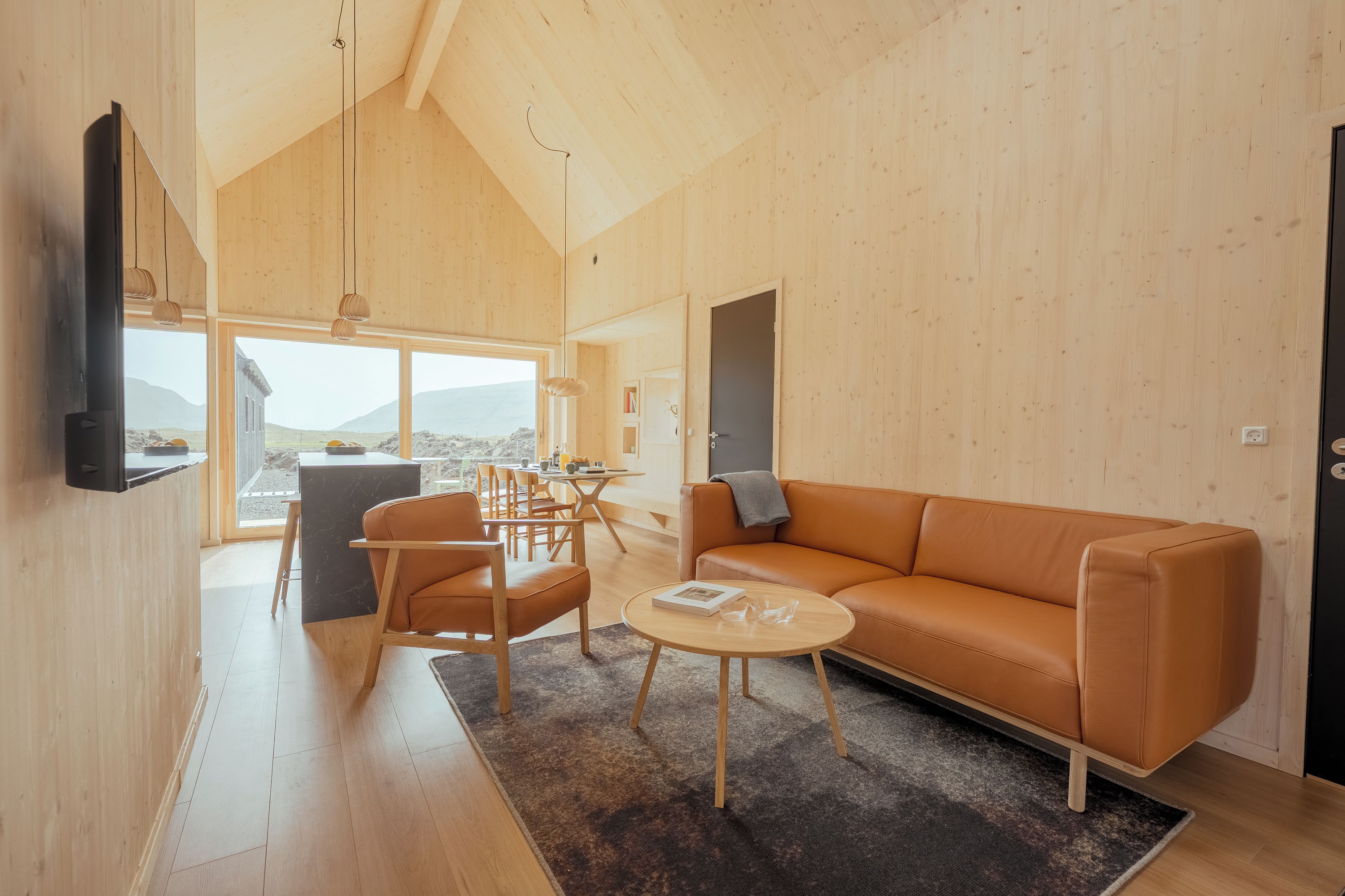 Un interior moderno con techo de madera, un sofá, sillas, una mesa de centro y vistas a través de amplios ventanales.