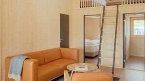 Ett rum i loftstil med ett träpanelat tak, en soffa, ett soffbord, en stege och en våningssäng.