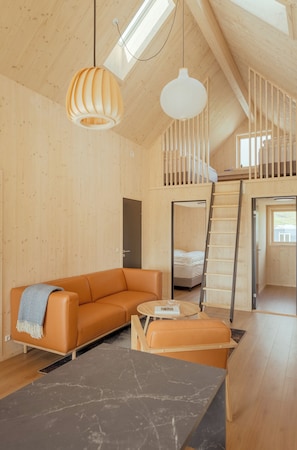 Habitación estilo loft con techo de madera, un sofá, una mesa de centro, una escalera y una cama individual sobre otra.