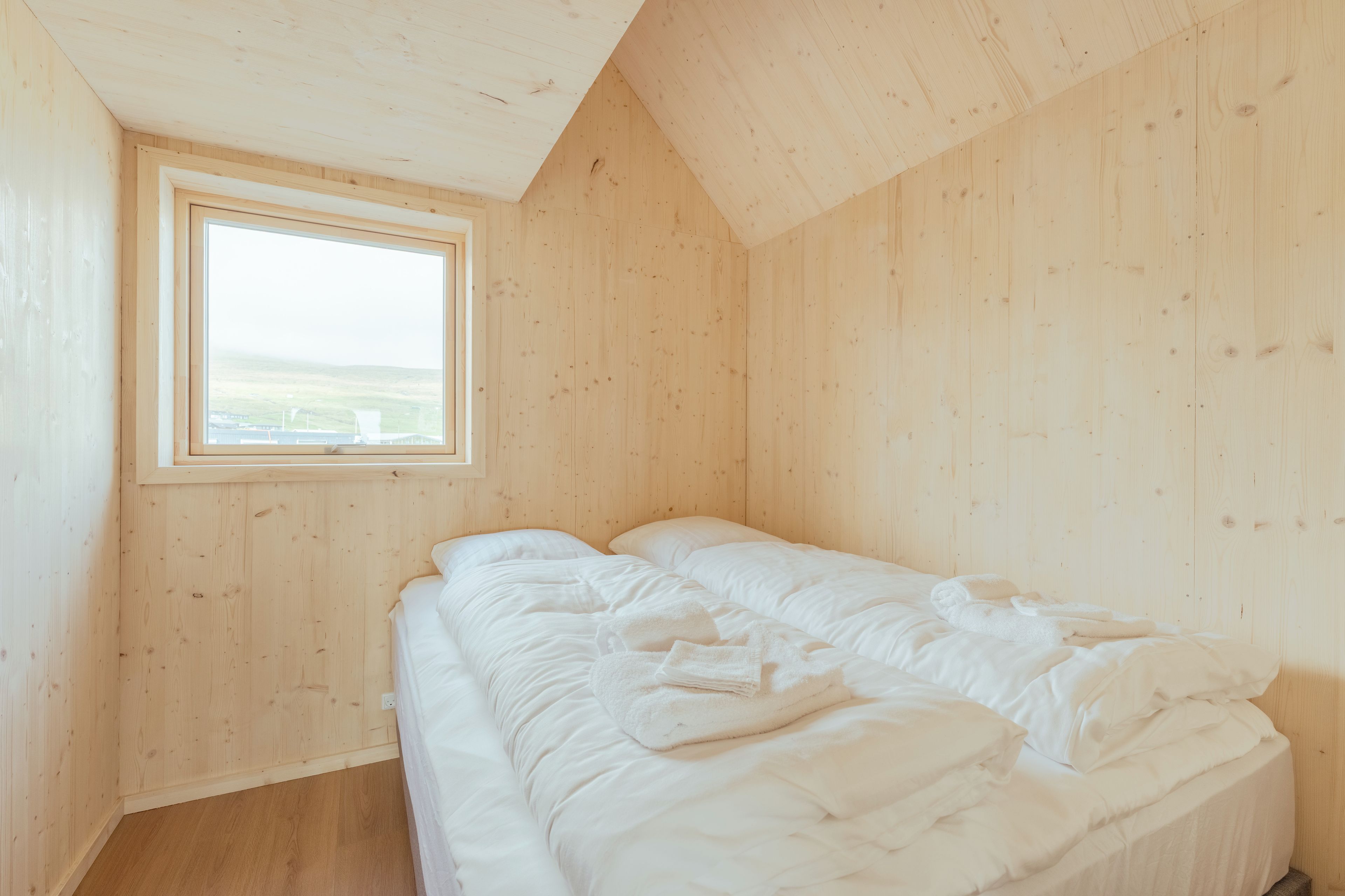 Ein Zimmer mit Holzwänden, einem Einzelbett mit weißer Bettwäsche und einem Dachfenster.