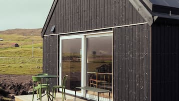 Un edificio moderno con techo inclinado, terraza de madera y puerta de cristal que da a un espacio interior.