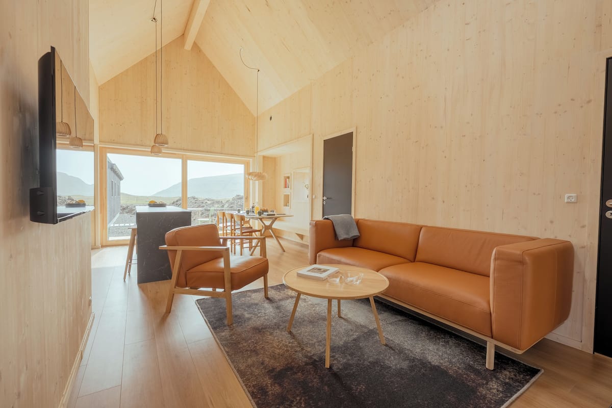 Un interior moderno con techo de madera, un sofá, sillas, una mesa de centro y vistas a través de amplios ventanales.