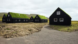 Una hilera de edificios negros con techos verdes, un sendero de grava y un paisaje montañoso.