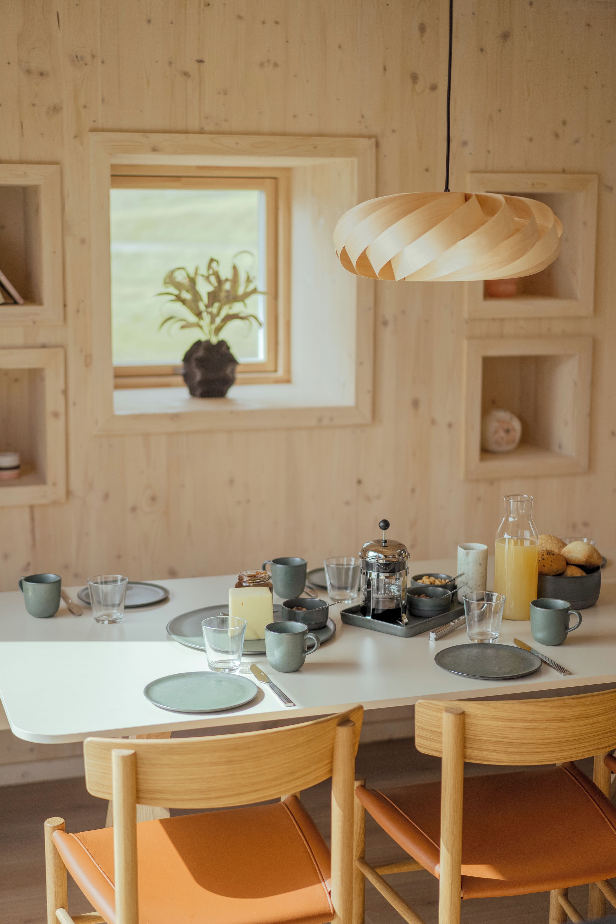 Una mesa de comedor de madera con platos, tazas y una botella, ubicada en una habitación con paredes de madera y una ventana.