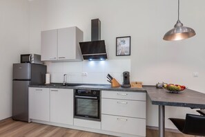 A modern kitchen with white cabinetry, a built-in oven, a coffee machine, and a fruit bowl on the counter.
