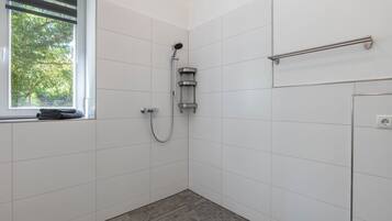 A small, modern bathroom with white tiles, a shower, a window with blinds, and a towel rack.