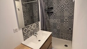 Un baño con lavamanos blanco, espejo y ducha con azulejos decorados.