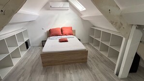 Un dormitorio con techo inclinado, una cama, estanterías blancas y un equipo de aire acondicionado.