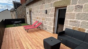 Un patio con suelo de madera, dos sillones rojos, un reposapiés negro y mobiliario de mimbre negro.