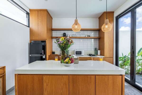 Uma cozinha moderna com armários de madeira, bancada branca, uma cesta de frutas e luminárias de vime suspensas.