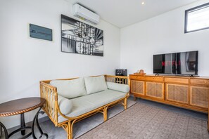 A room with a wicker sofa, a small table, a TV, and a cabinet. - VILLA TRATASAN CANGGU (Badung)