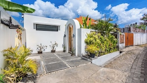 A white building with a wooden door, potted plants, and a paved entrance. - VILLA TRATASAN CANGGU (Badung)