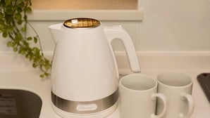 Een witte elektrische waterkoker met een gouden deksel en twee witte mokken op een aanrecht.