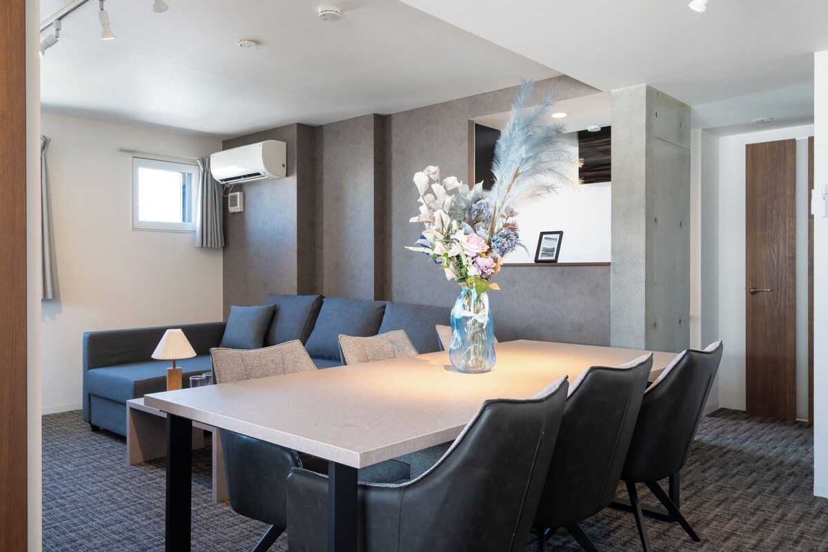 A modern hotel room with a dining area, a sofa, and a decorative vase with flowers.