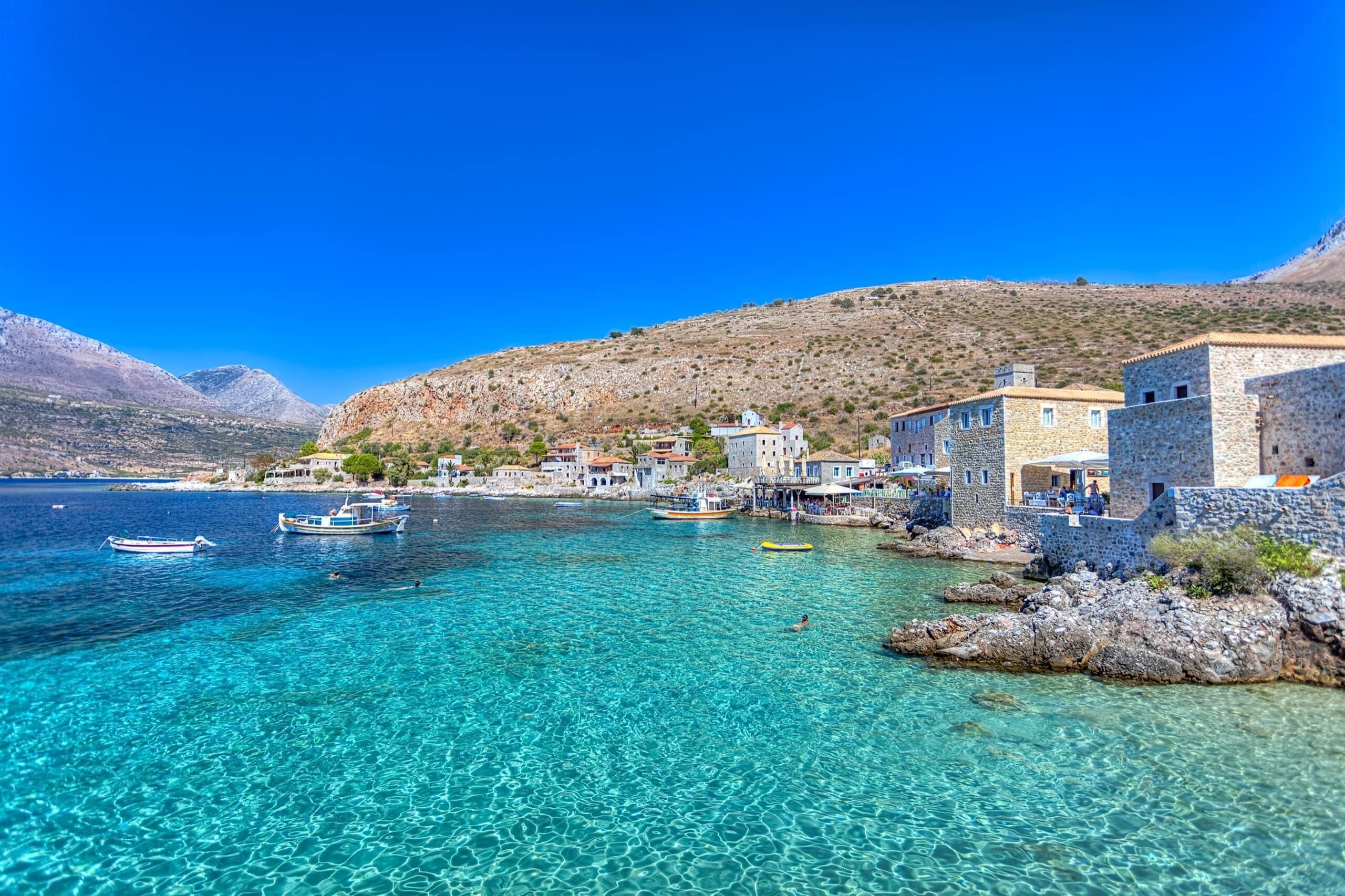 A coastal village with clear turquoise waters, stone buildings, and boats.