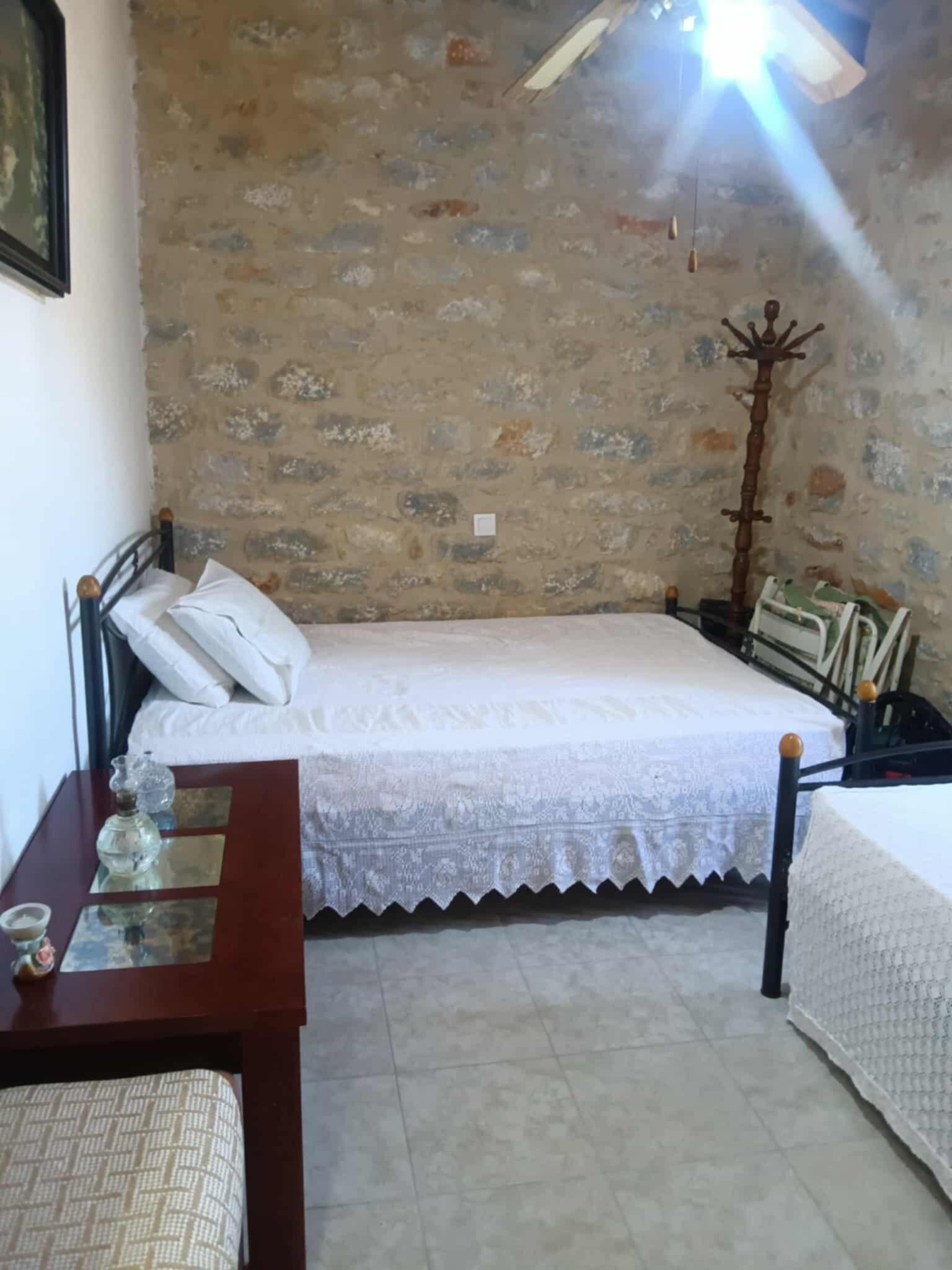 Una camera da letto con parete in pietra, un letto con biancheria bianca, un comodino in legno e un tavolino da notte con una lampada e un piccolo oggetto decorativo.